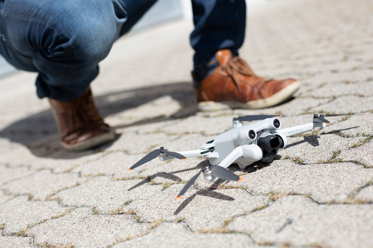 Mini 3 Pro Drohne auf dem Vorplatz mit Füssen im  Hintergrund.