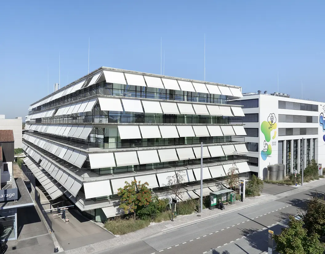 Das Gebäude H89 auf dem SONUVO-Campus in Allschwil von schräg oben, gestaffelte Fassade vor blauem Himmel