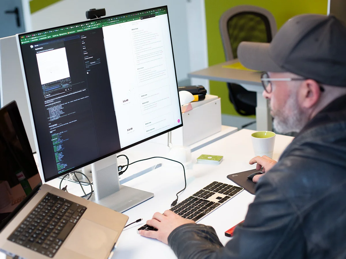Patrick arbeitet mit Cap am Schreibtisch, auf dem Bildschirm Code und Layout