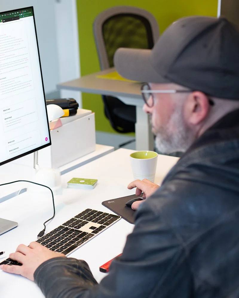 Patrick arbeitet mit Cap am Schreibtisch, auf dem Bildschirm Code und Layout