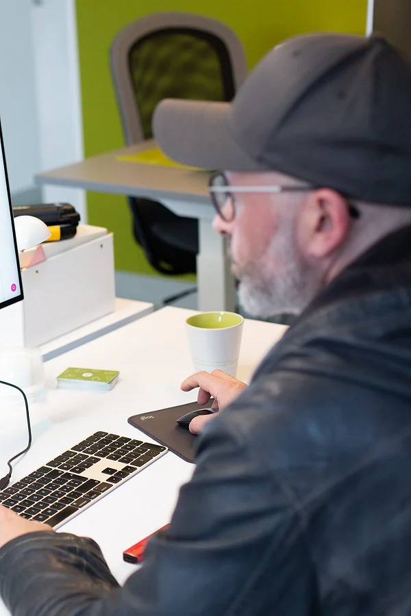 Patrick arbeitet mit Cap am Schreibtisch, auf dem Bildschirm Code und Layout