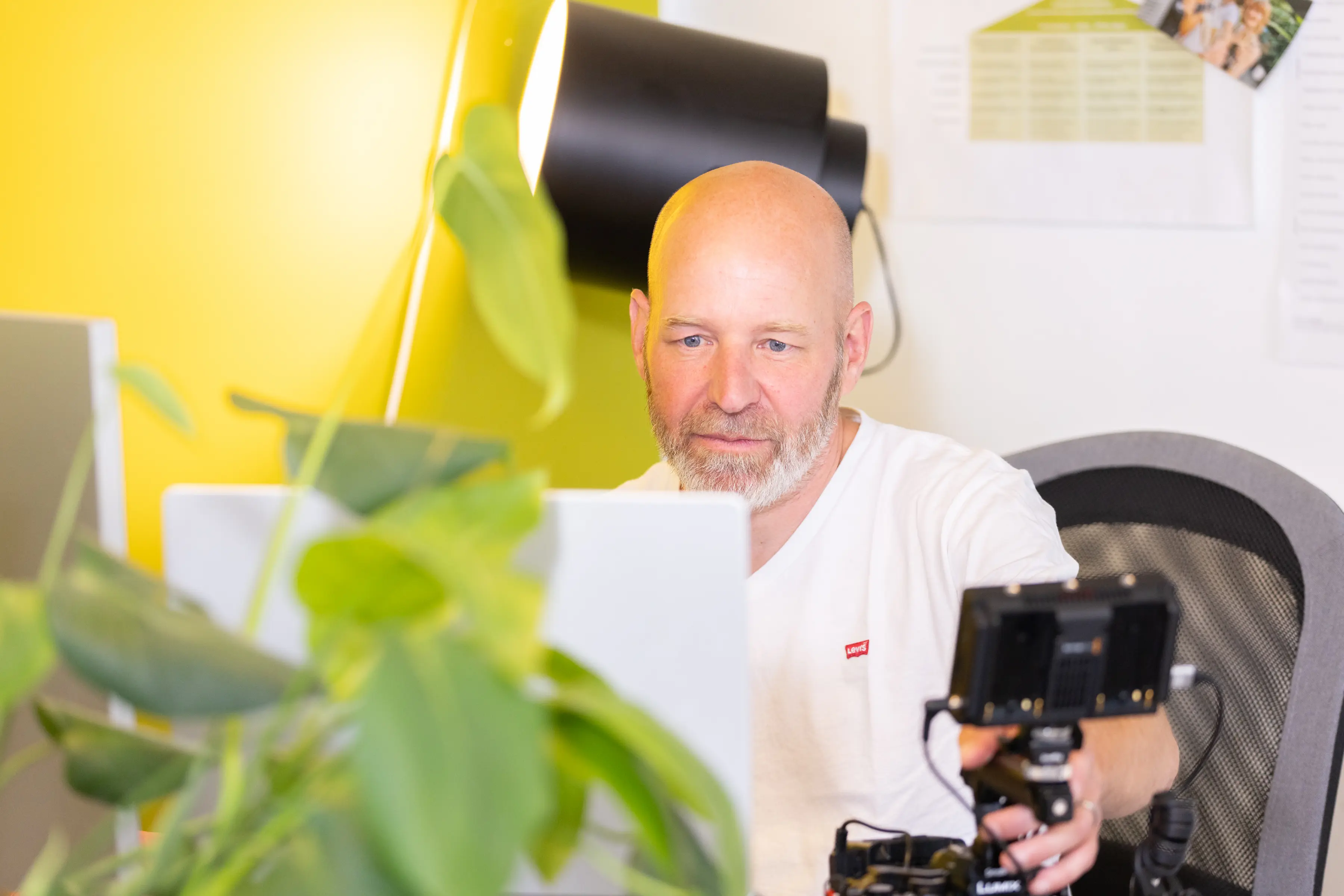 Roger am Schreibtisch mit Kamera-Rig vor der gelben Wand