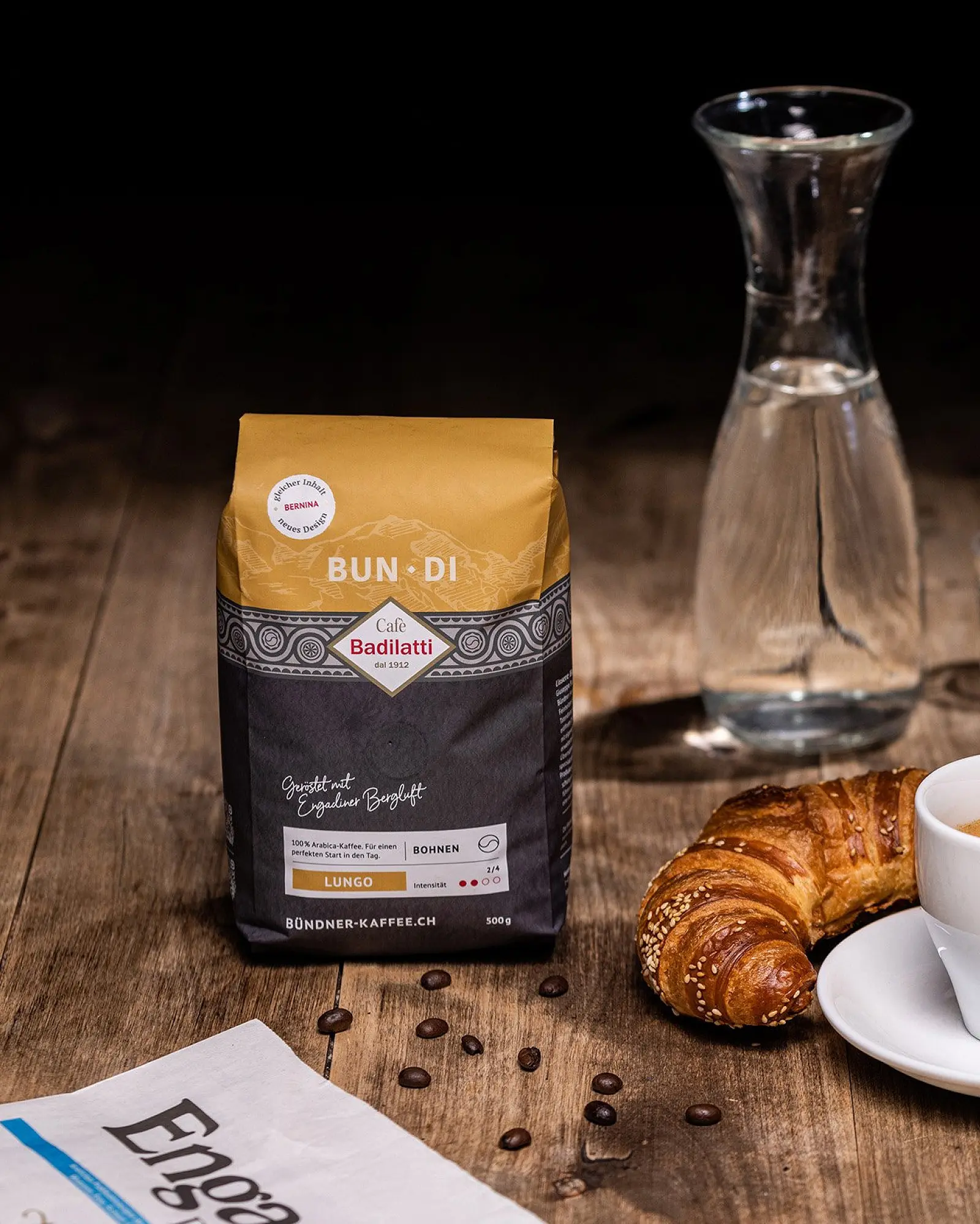 Kaffeepackung «Bun·Di» neben Karaffe, Gipfeli und Tasse auf einem Holztisch