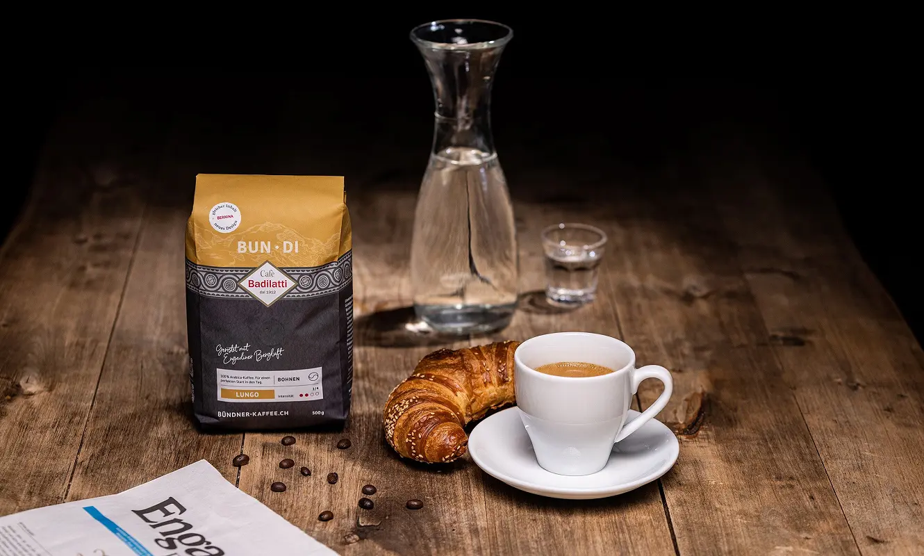 Kaffeepackung «Bun·Di» neben Karaffe, Gipfeli und Tasse auf einem Holztisch