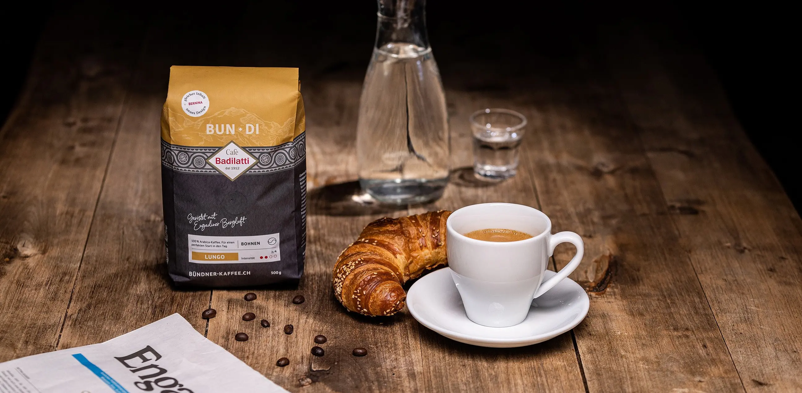 Kaffeepackung «Bun·Di» neben Karaffe, Gipfeli und Tasse auf einem Holztisch