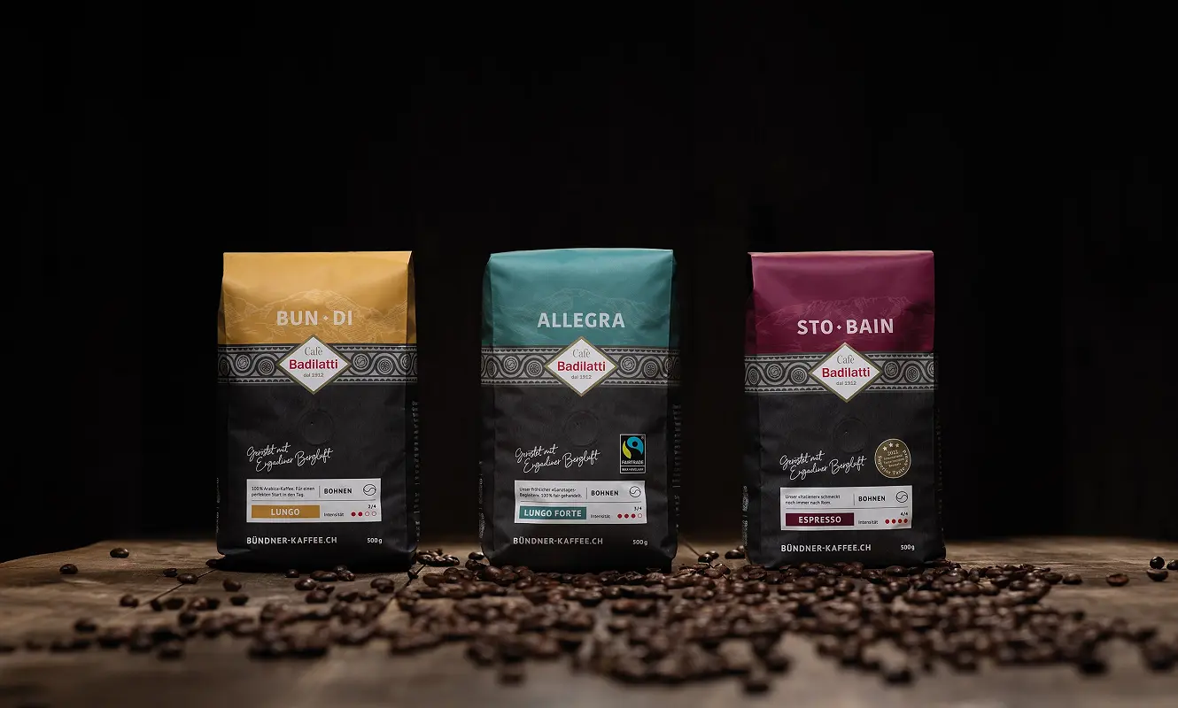 Drei Kaffeepackungen nebeneinander: «Bun·Di», «Allegra» und «Sto·Bain» vor gestreuten Bohnen