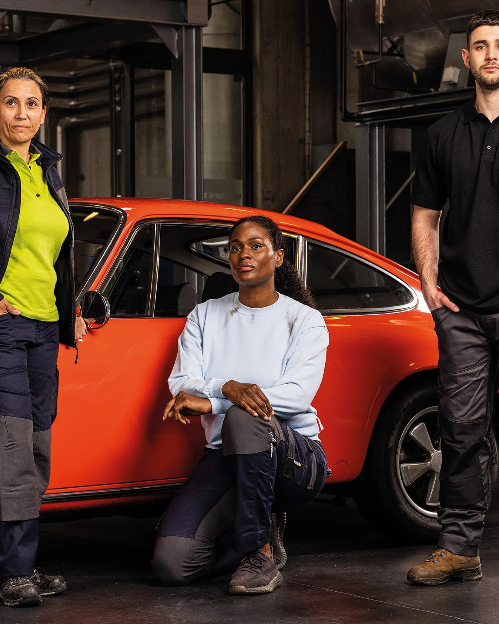 Drei Personen in Arbeitskleidung vor einem roten Oldtimer in der Werkstatt