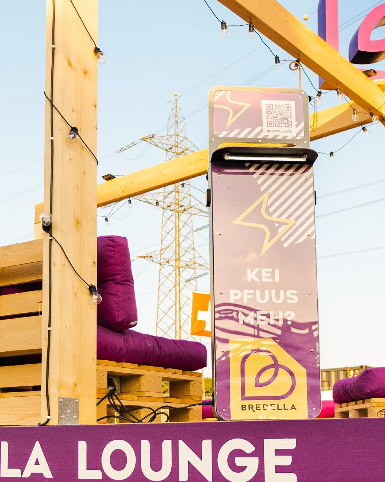 Holzrahmen der Bredella Lounge mit Signet, davor die Stele «Kei Pfuus meh?» und die violette Sockelblende