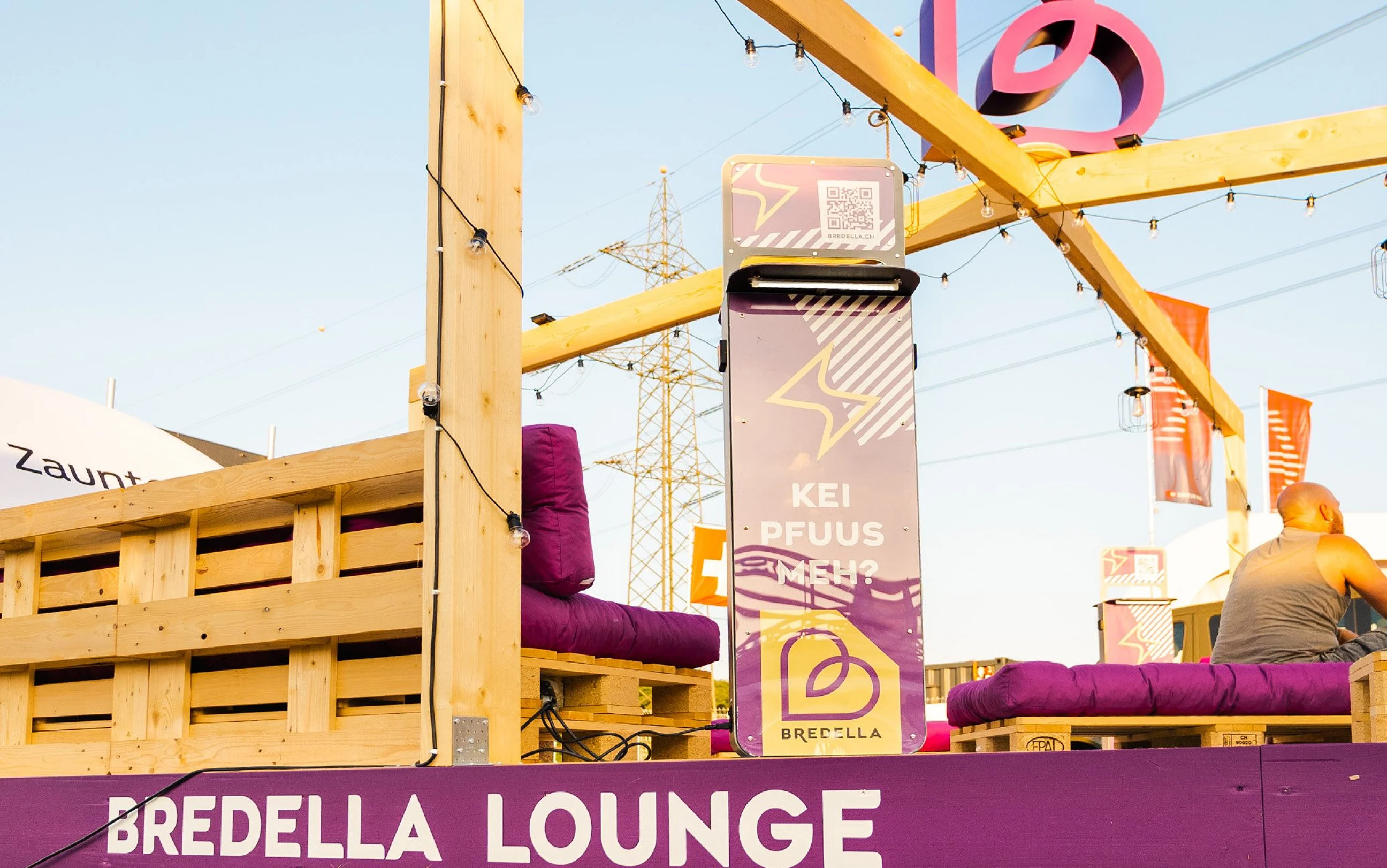 Holzrahmen der Bredella Lounge mit Signet, davor die Stele «Kei Pfuus meh?» und die violette Sockelblende