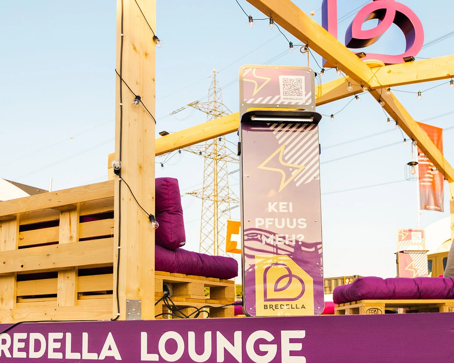 Holzrahmen der Bredella Lounge mit Signet, davor die Stele «Kei Pfuus meh?» und die violette Sockelblende