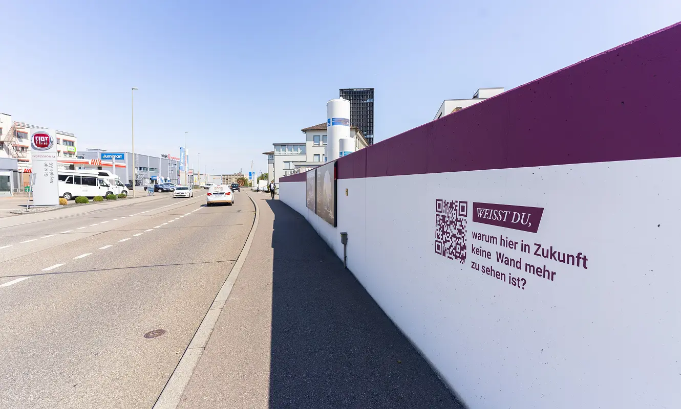 Station des Areal-Rundgangs entlang der Strasse: QR-Code neben der Frage «Weisst du, warum hier in Zukunft keine Wand mehr zu sehen ist?»