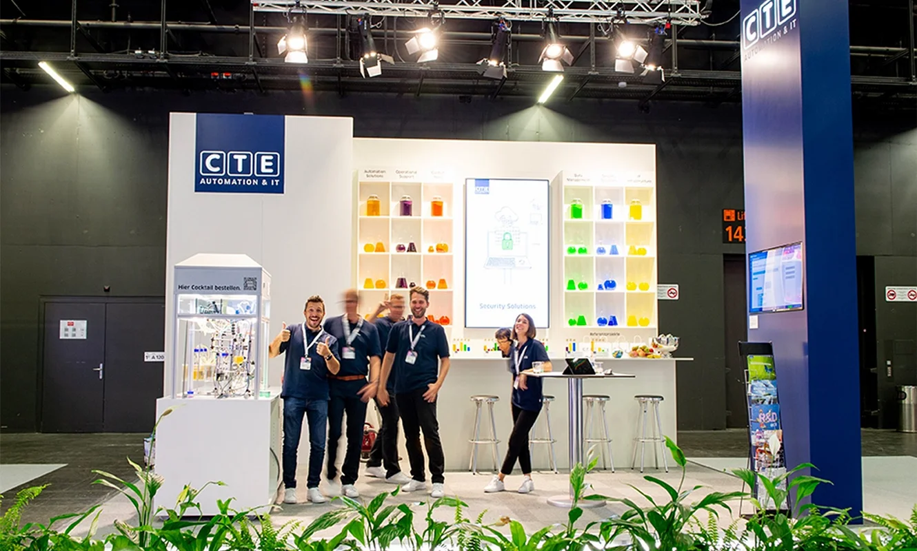 CTE-Messestand an der Ilmac 2023 in Basel: links die Cocktailmaschine im Glaskubus, in der Mitte die Regalwand mit farbigen Gefässen und Bildschirm, rechts der blaue Turm mit dem CTE-Logo