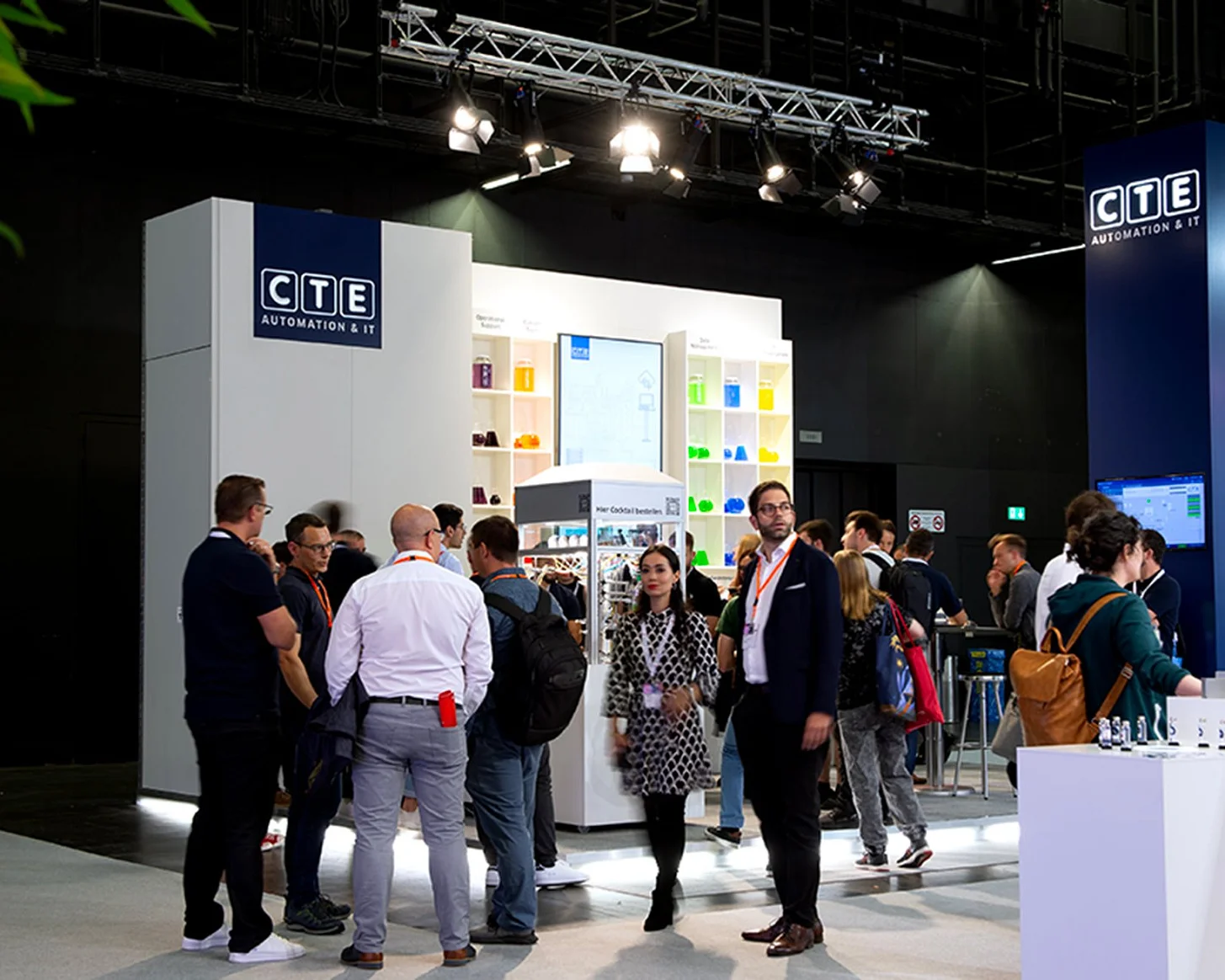 Betrieb am CTE-Stand an der Ilmac 2023: Besucherinnen und Besucher stehen vor der Regalwand und dem Cocktailkubus, rechts der blaue Turm mit dem Logo