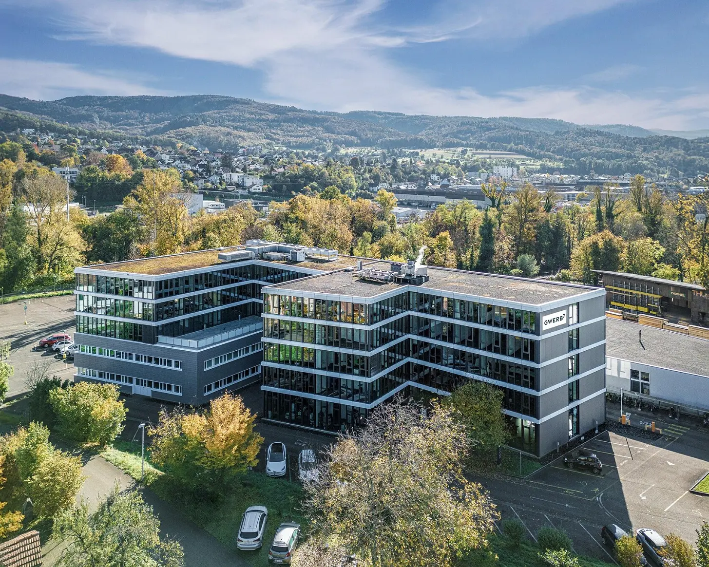 Drohnenaufnahme des GWERB7 in Aesch mit Fassadenschriftzug, begrüntem Dach und Blick über das Birstal