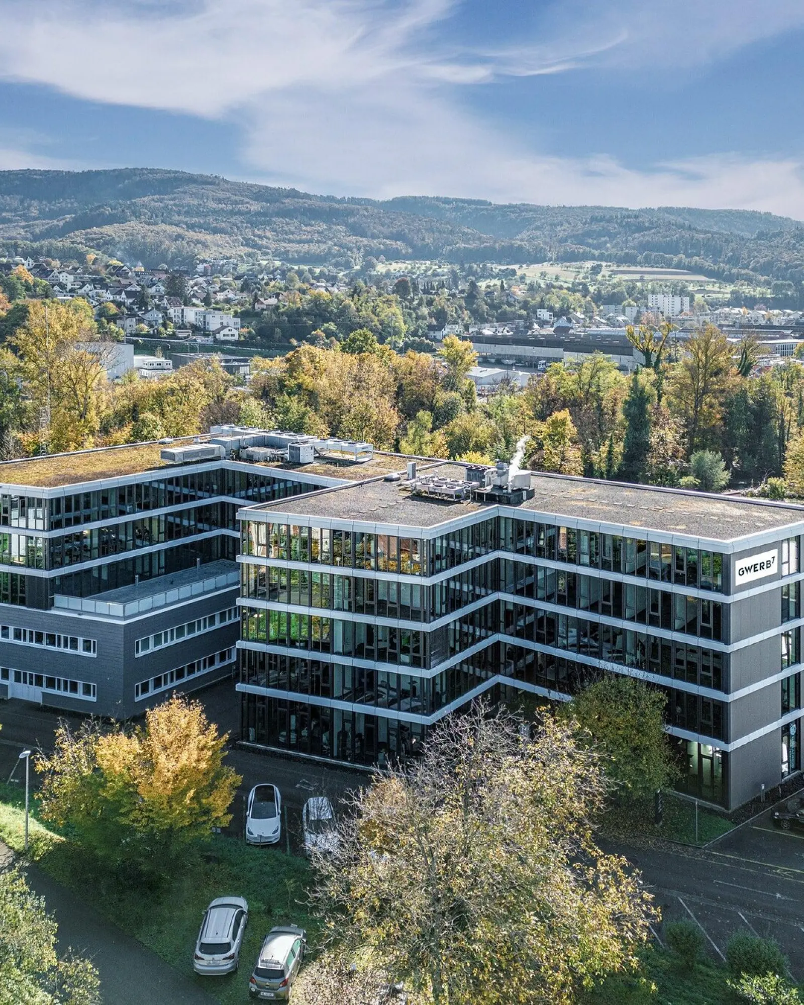 Drohnenaufnahme des GWERB7 in Aesch mit Fassadenschriftzug, begrüntem Dach und Blick über das Birstal