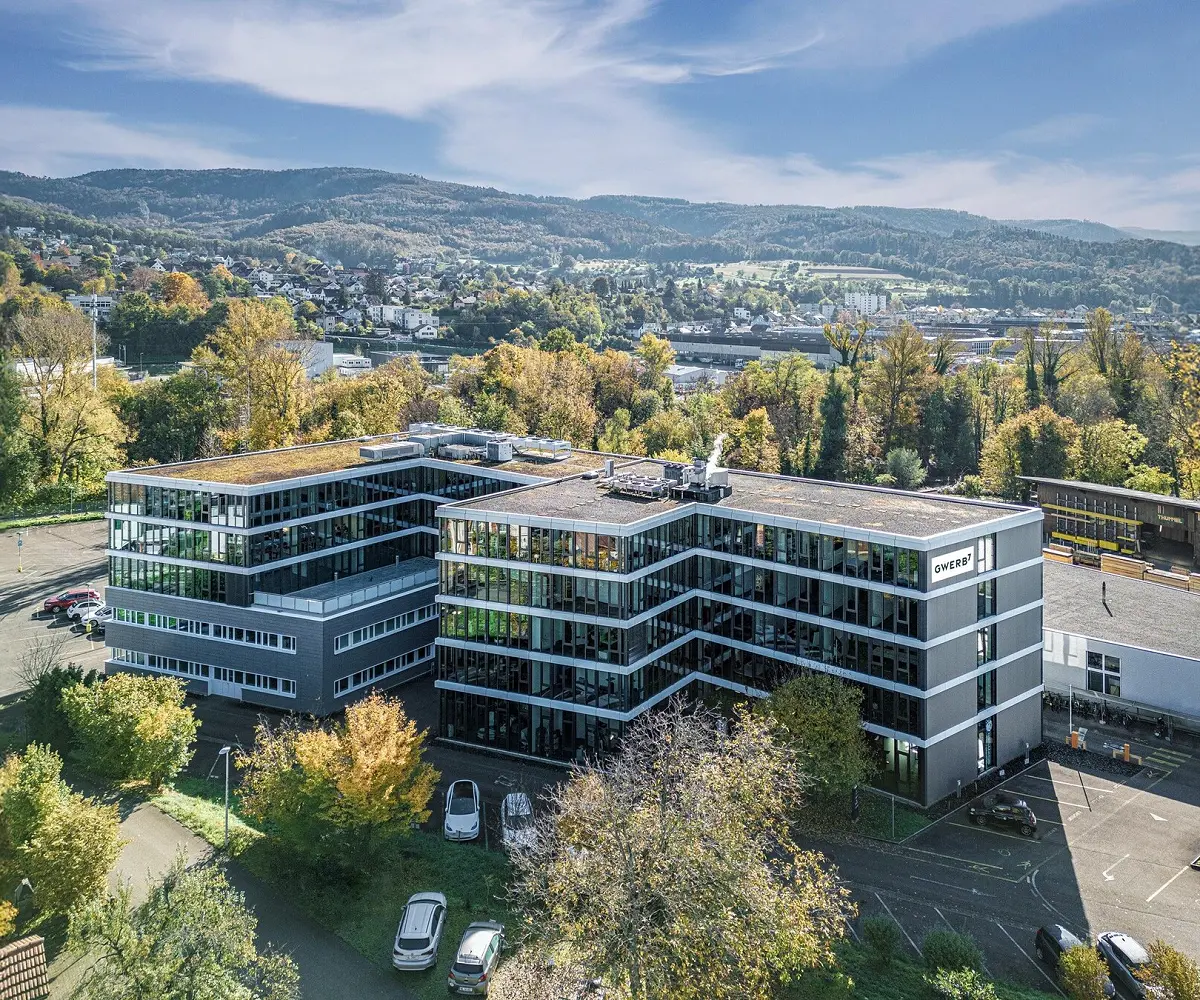 Drohnenaufnahme des GWERB7 in Aesch mit Fassadenschriftzug, begrüntem Dach und Blick über das Birstal