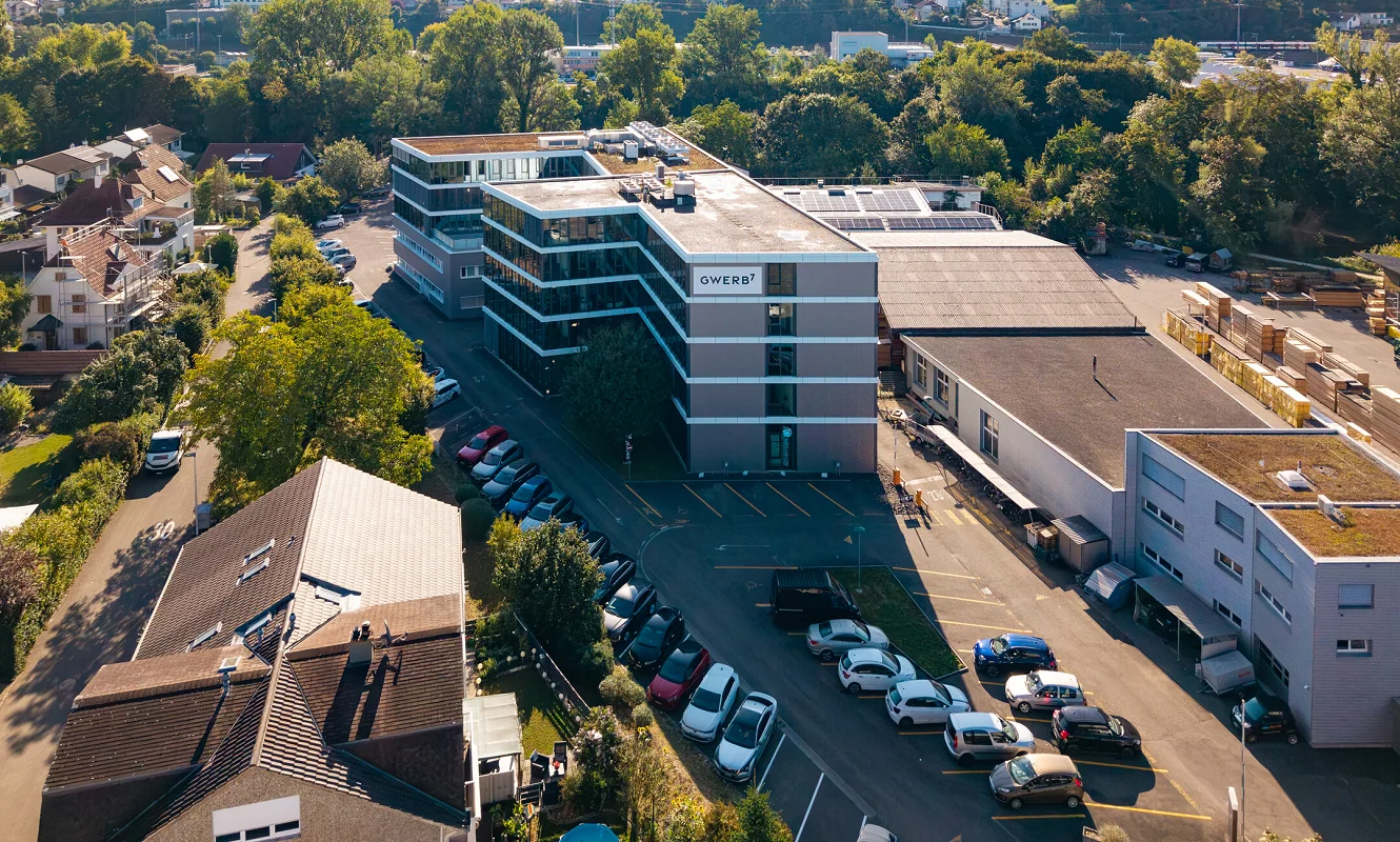Drohnenaufnahme des Gewerbegebiets in Aesch mit dem GWERB7-Gebäude, Parkplatz und Nachbarbauten