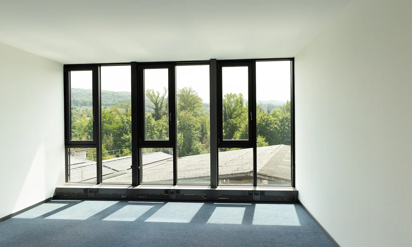 Leerer Raum mit bodentiefer Fensterfront und Blick ins Grüne