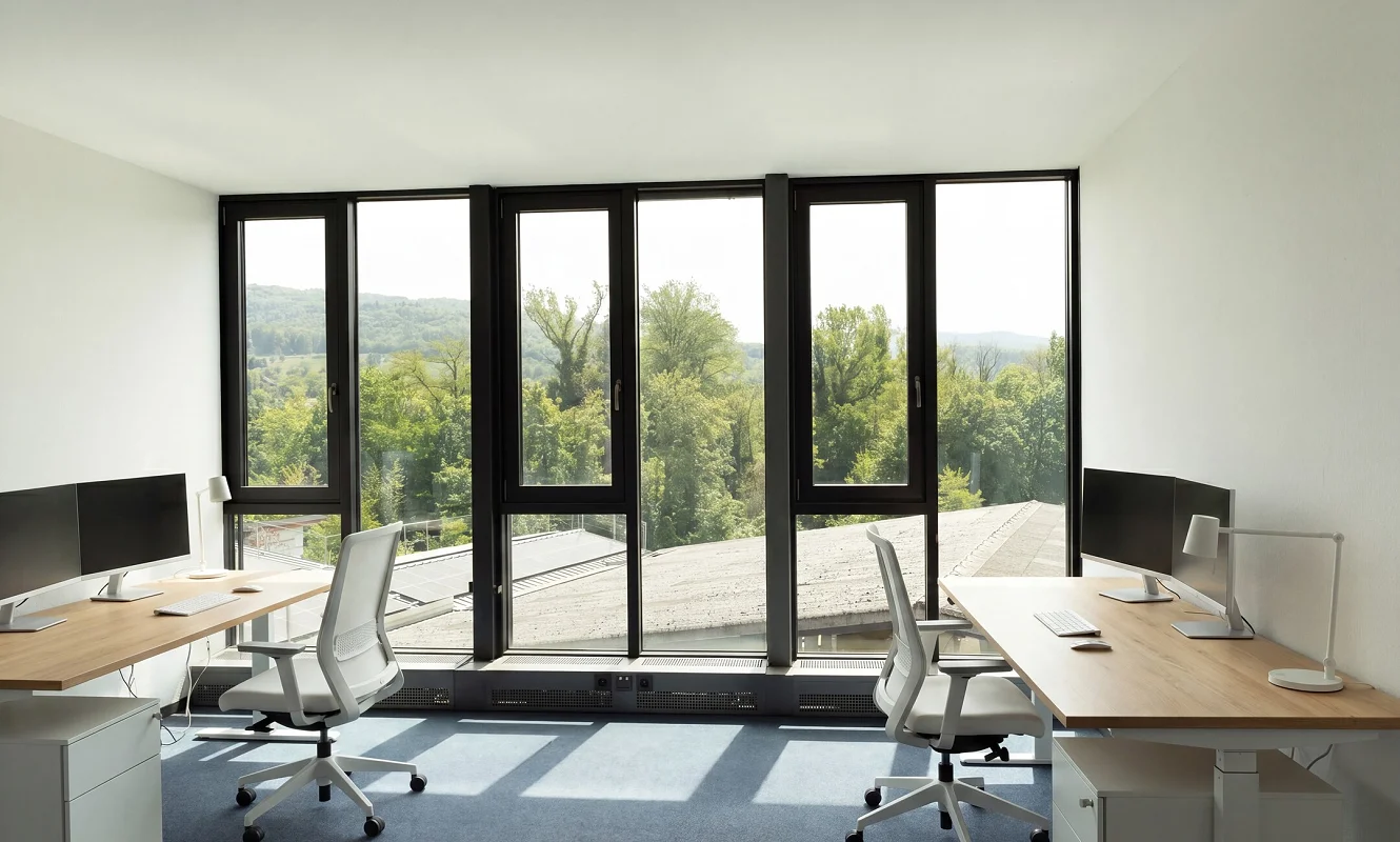 Eingerichtetes Büro mit hellen Schreibtischen, Stühlen und Blick auf Bäume