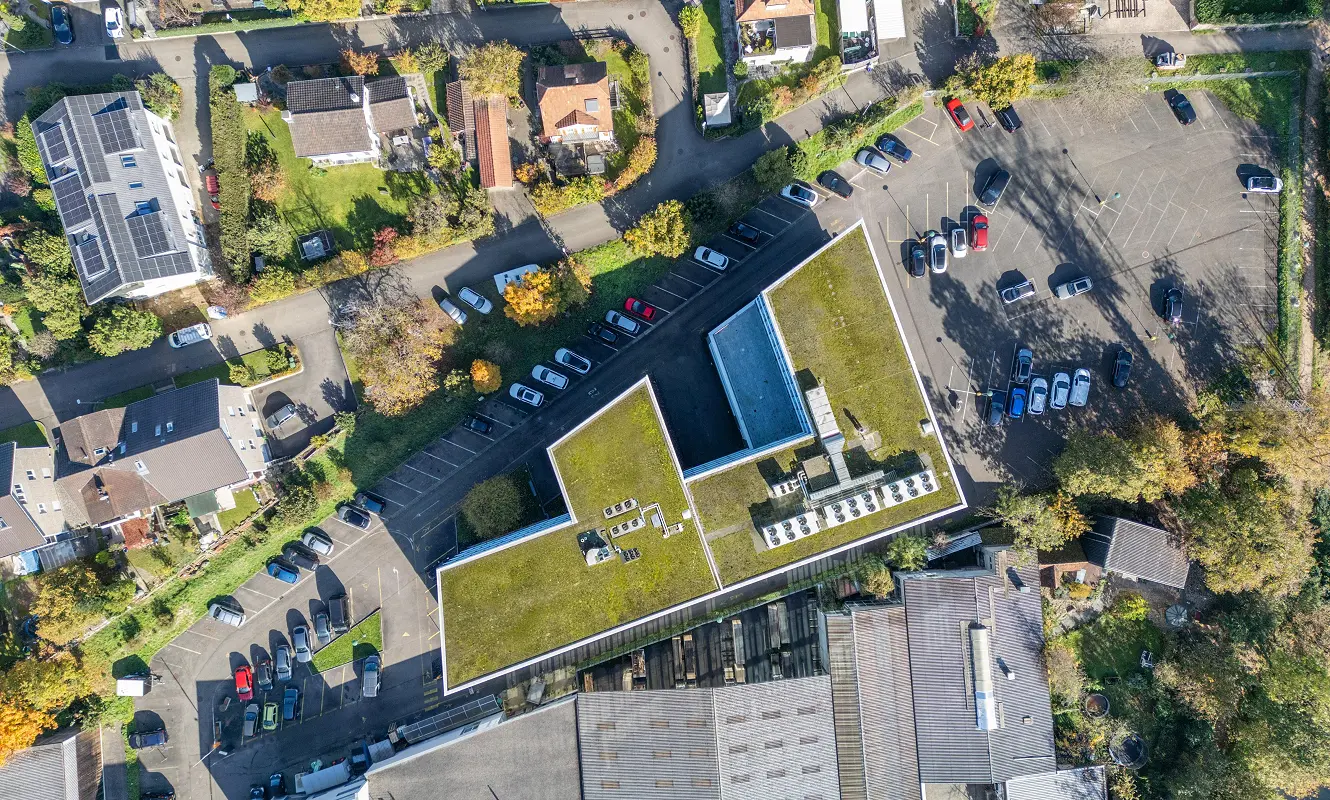 Senkrechte Drohnenaufnahme des GWERB7 mit begrüntem Flachdach, Parkplätzen und angrenzendem Wohnquartier in Aesch