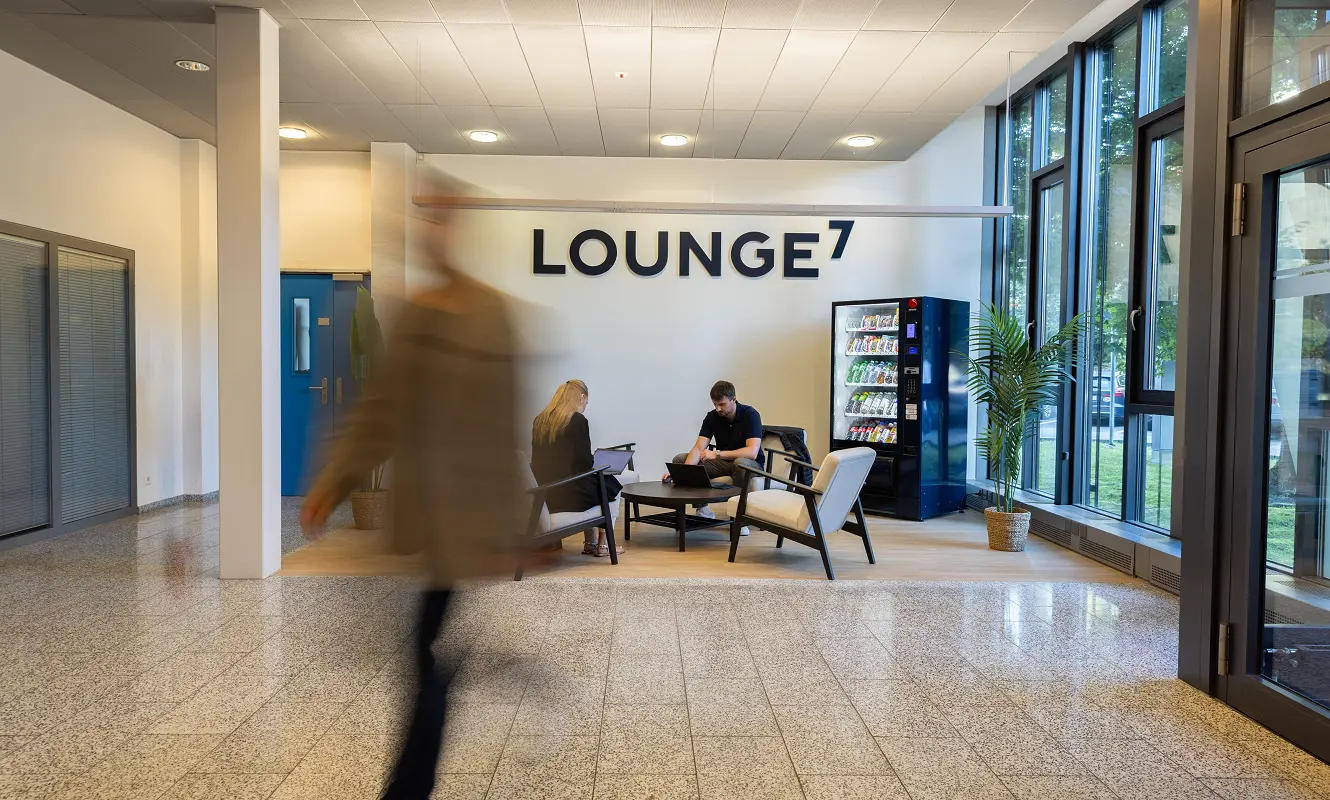 Lounge7 im GWERB7: Wandschriftzug, Sitzgruppe mit zwei Arbeitenden am Laptop und Snackautomat