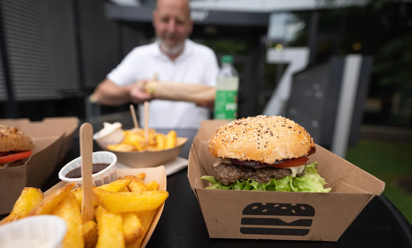 Burger und Pommes frites in Kartonschalen, im Hintergrund ein Gast