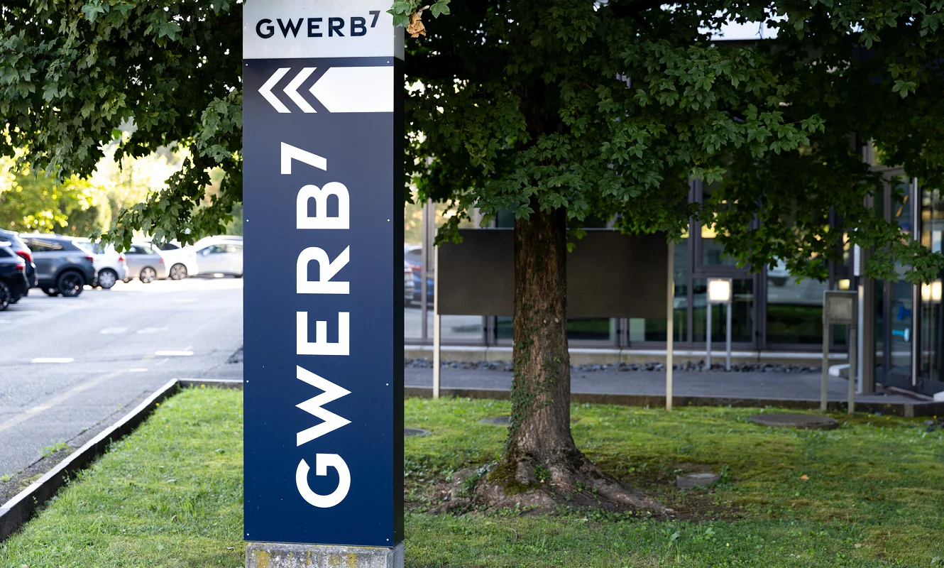 Pylon mit GWERB7-Beschriftung und Richtungspfeil vor dem Gebäude