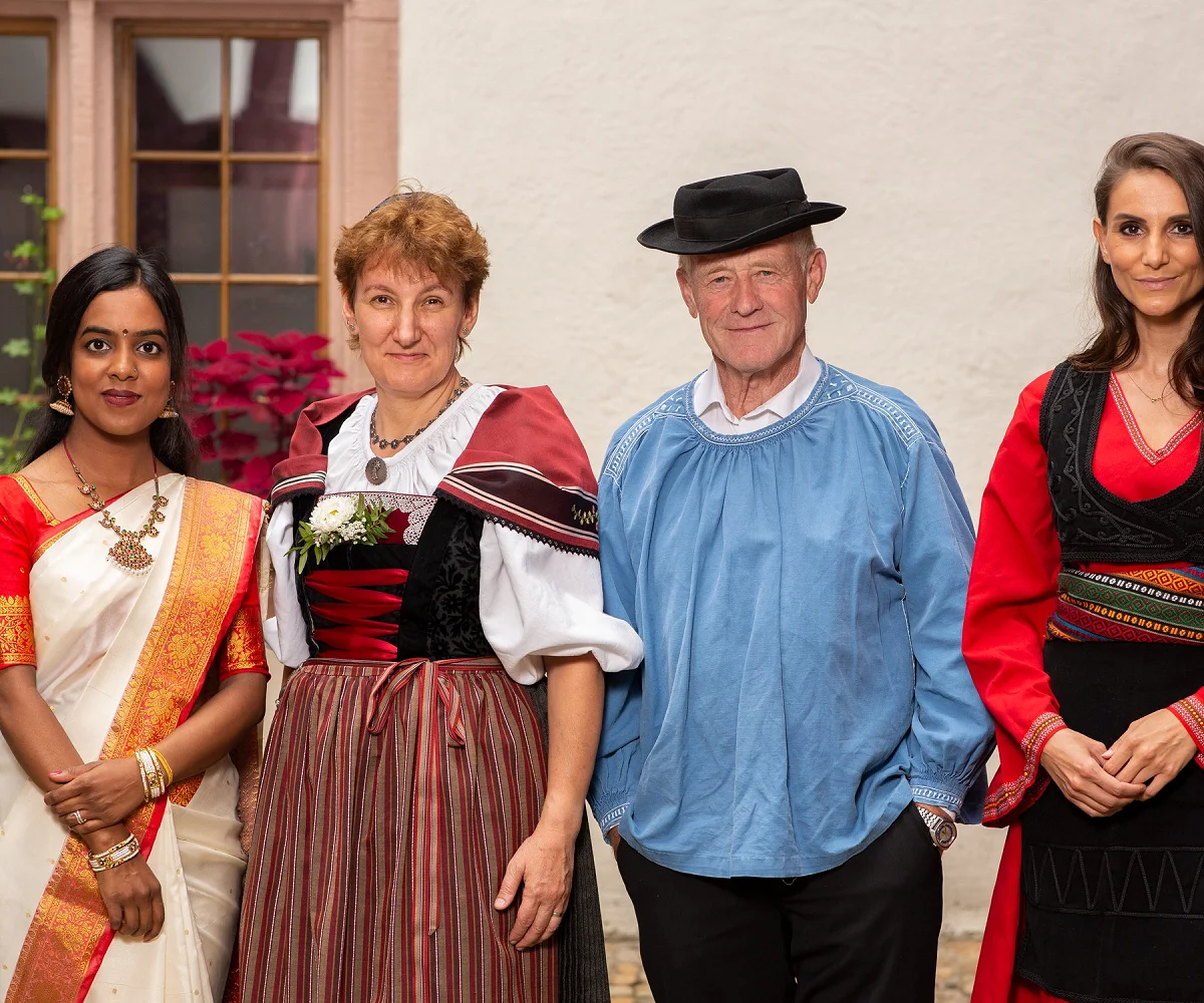 Vier Menschen in Trachten aus verschiedenen Kulturen stehen nebeneinander in einem Innenhof