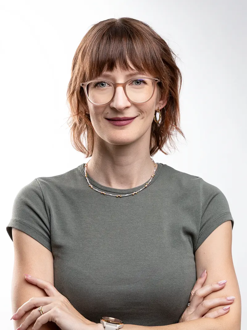Porträt von Hanna mit verschränkten Armen im olivgrünen Shirt vor hellem Hintergrund